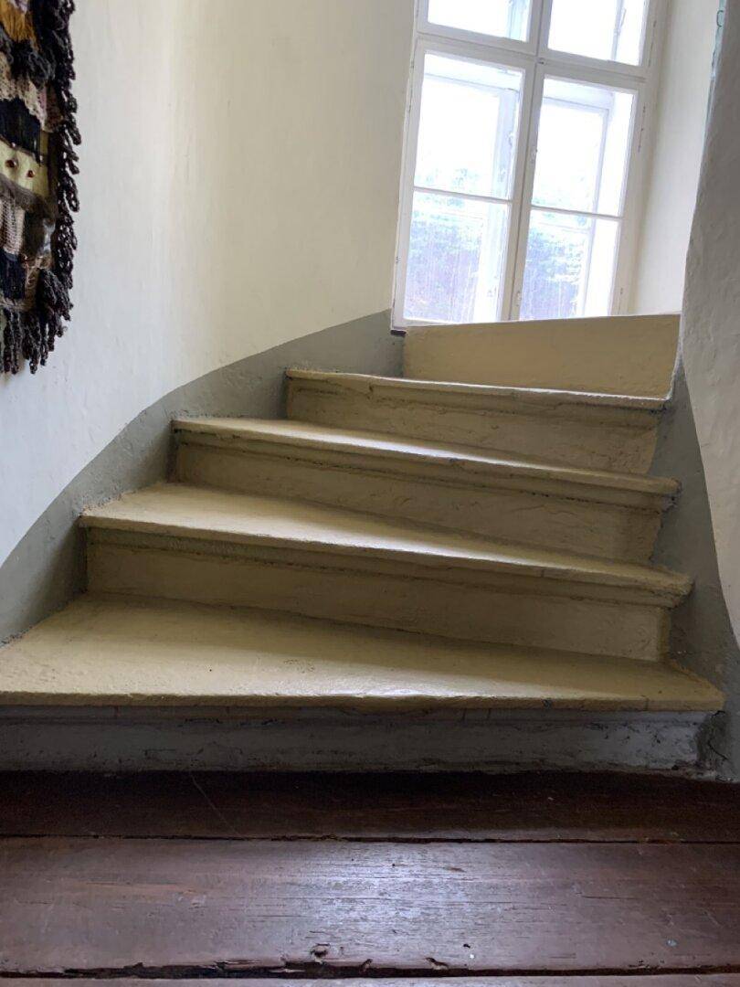 Geschwungene Steintreppe mit einem Fenster in einem historischen Gebäude.