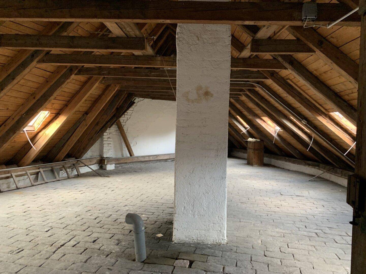 Großer Dachboden mit Holzbalken, Dachfenstern und einem zentralen Pfeiler.
