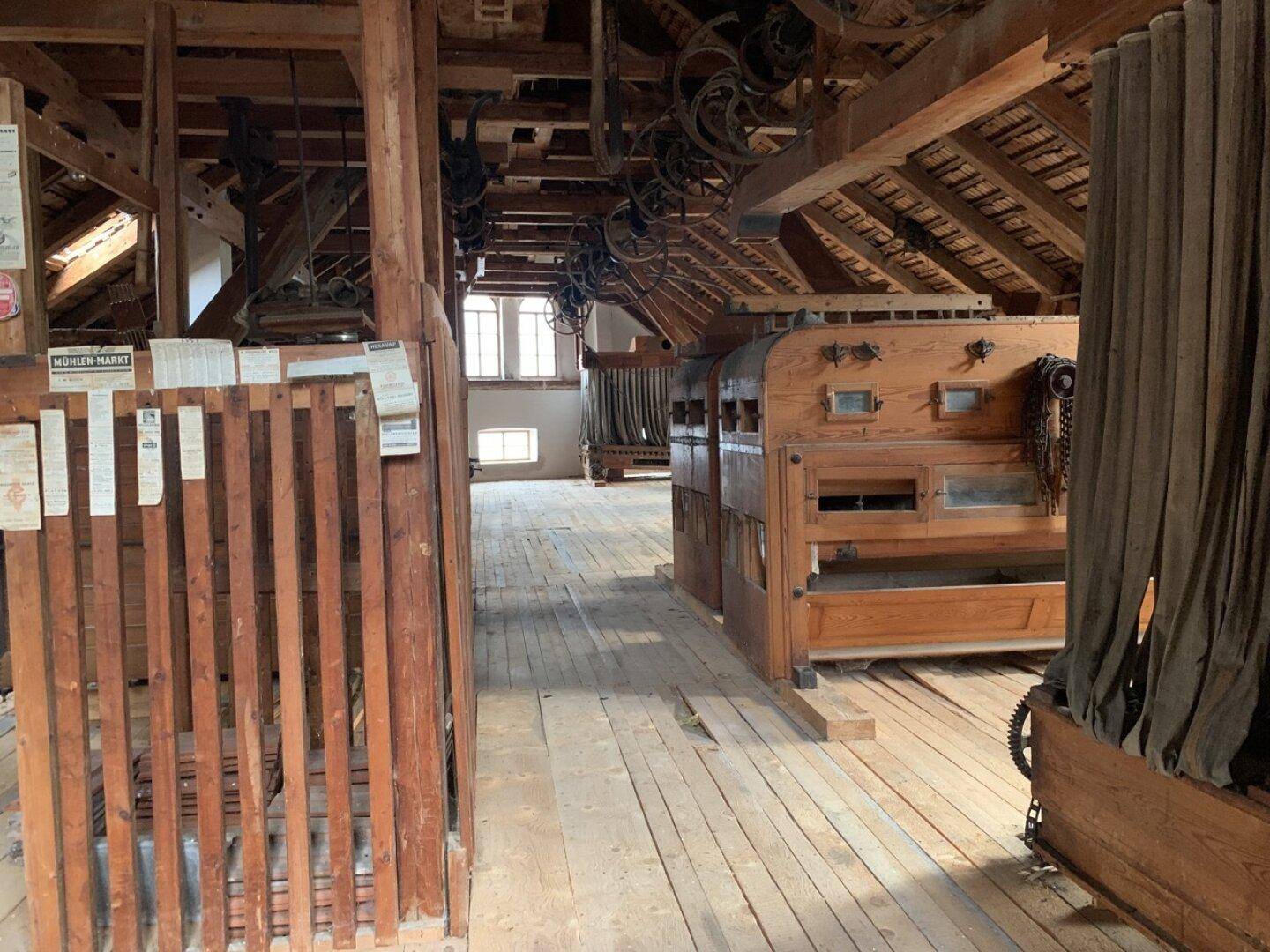Historischer Mühlenraum mit alten Maschinen, Holzbalken und Holzboden.