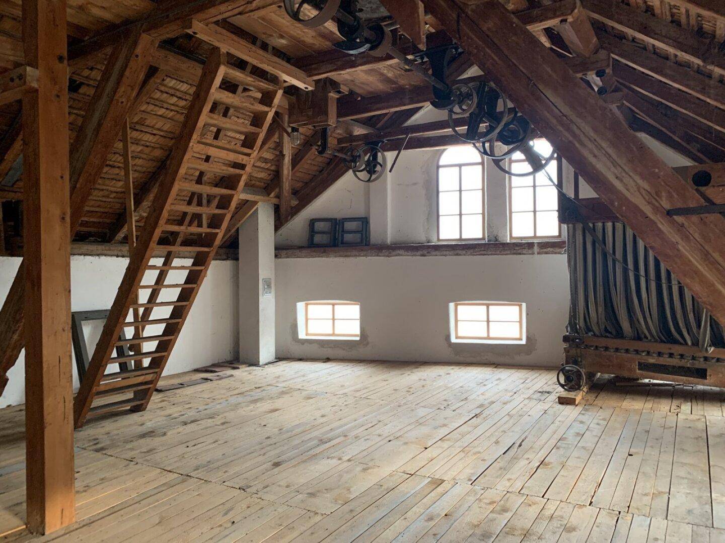 Großer Mühlenraum mit Holzbalken, alten Maschinen und Fenstern.