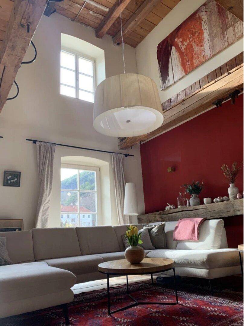 Lichtdurchflutetes Wohnzimmer mit hohen Decken, Holzbalken und einer roten Akzentwand.