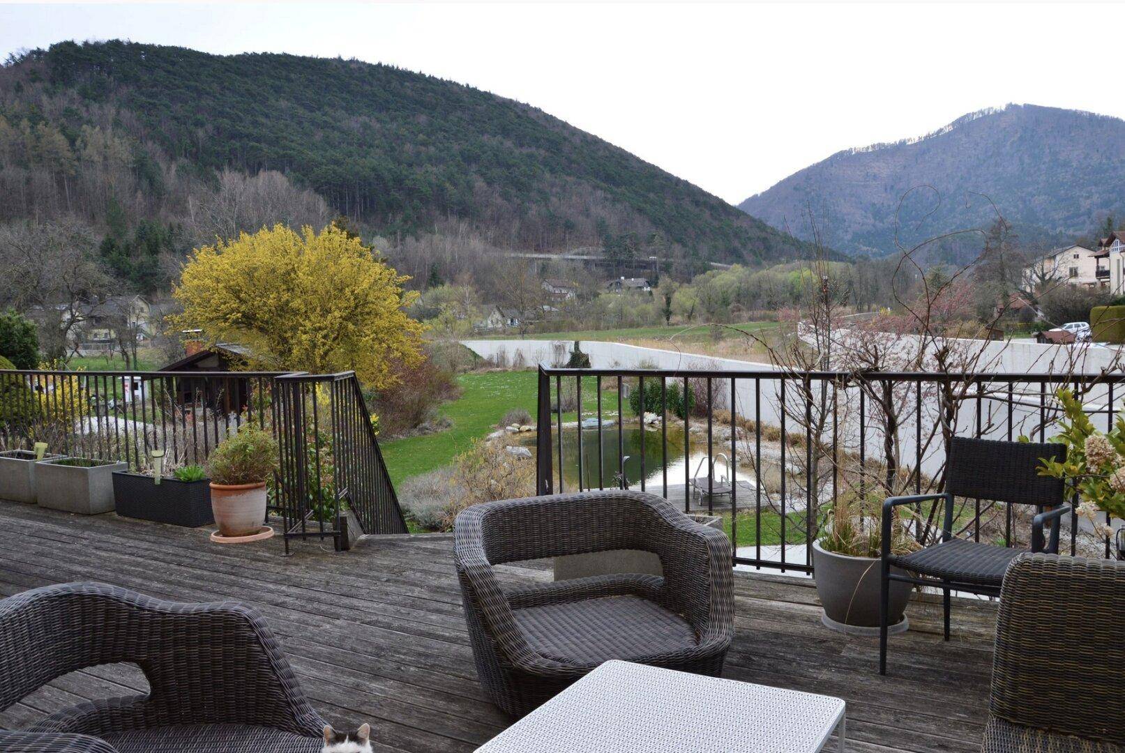 Geräumige Terrasse mit Korbmöbeln und weitem Blick auf die Berge und einen Teich.