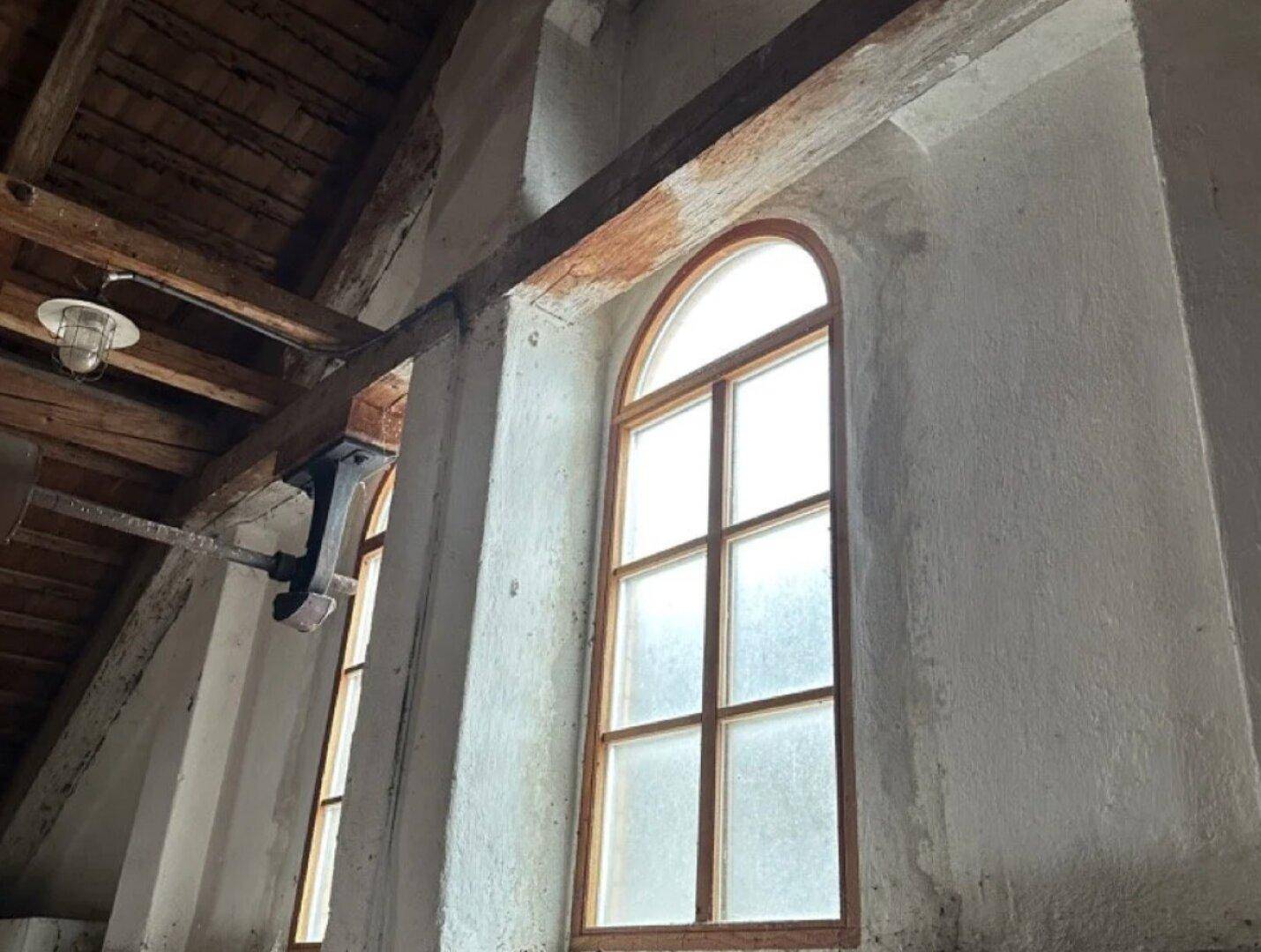Gewölbtes Fenster und Holzbalkendecke in einem historischen Raum.
