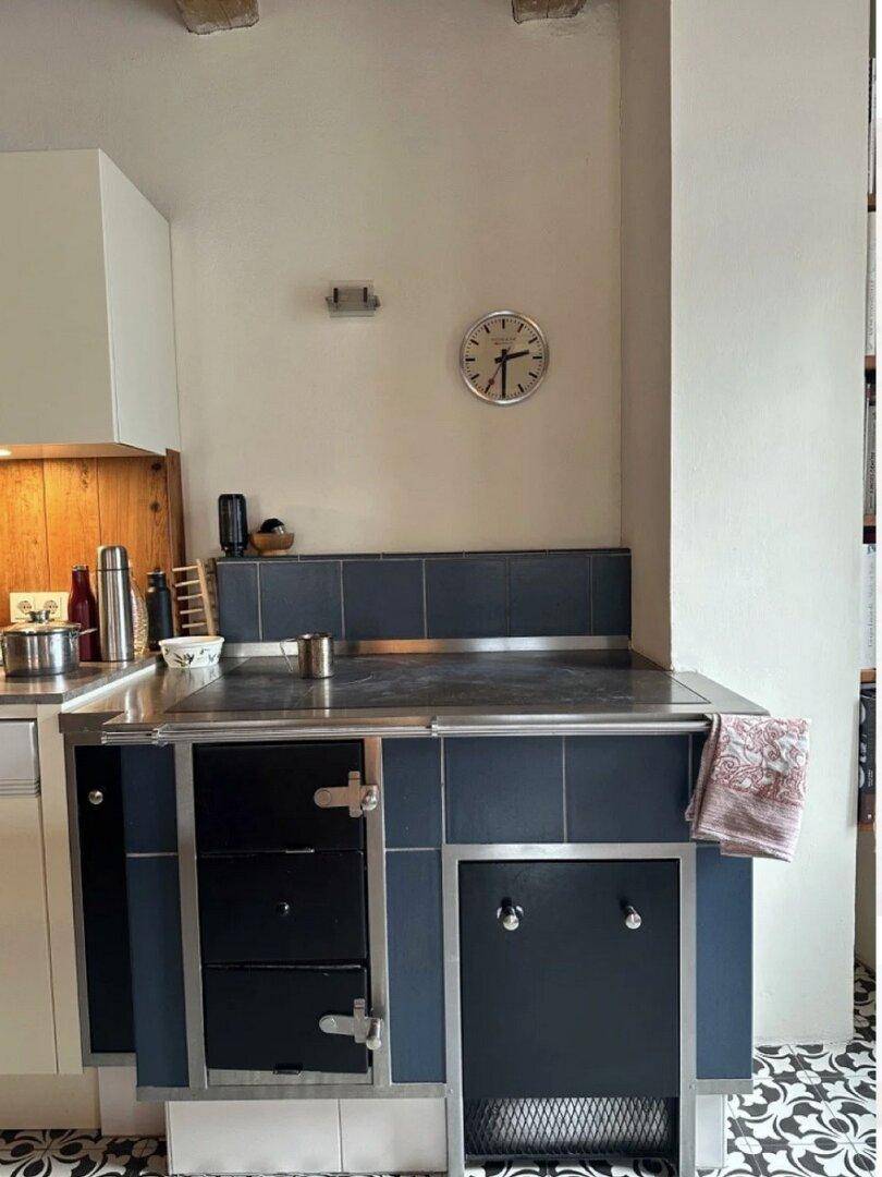 Rustikale Küche mit einem blauen Holzofen und gemusterten Bodenfliesen.