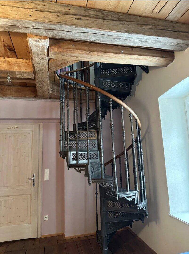 Detailansicht einer kunstvollen gusseisernen Wendeltreppe mit Holzhandlauf.