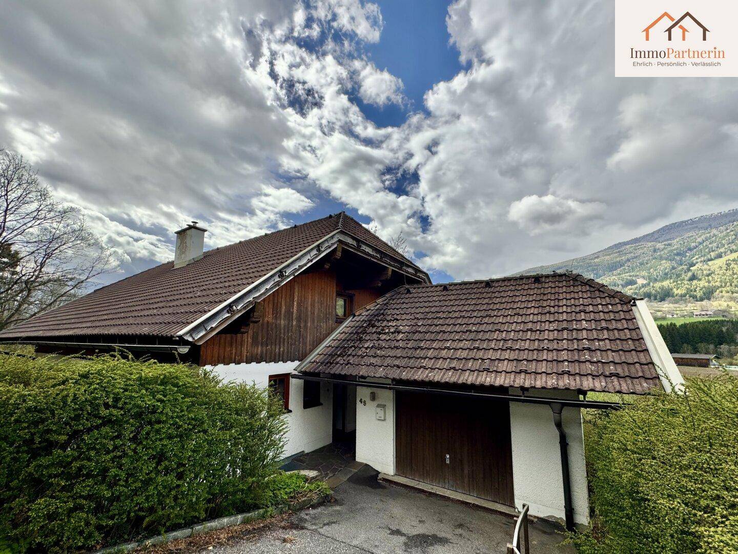 Hausansicht mit integrierter Garage und traditionellem Satteldach in bergiger Umgebung.