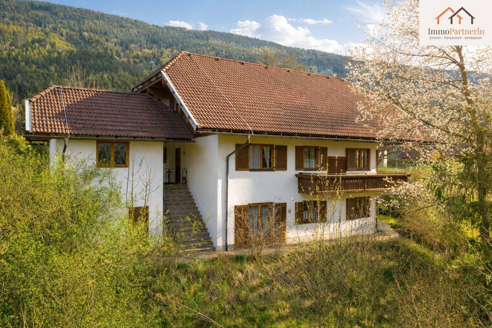 Seitenansicht des Hauses mit Außentreppe und Balkon, eingebettet in eine grüne Landschaft.