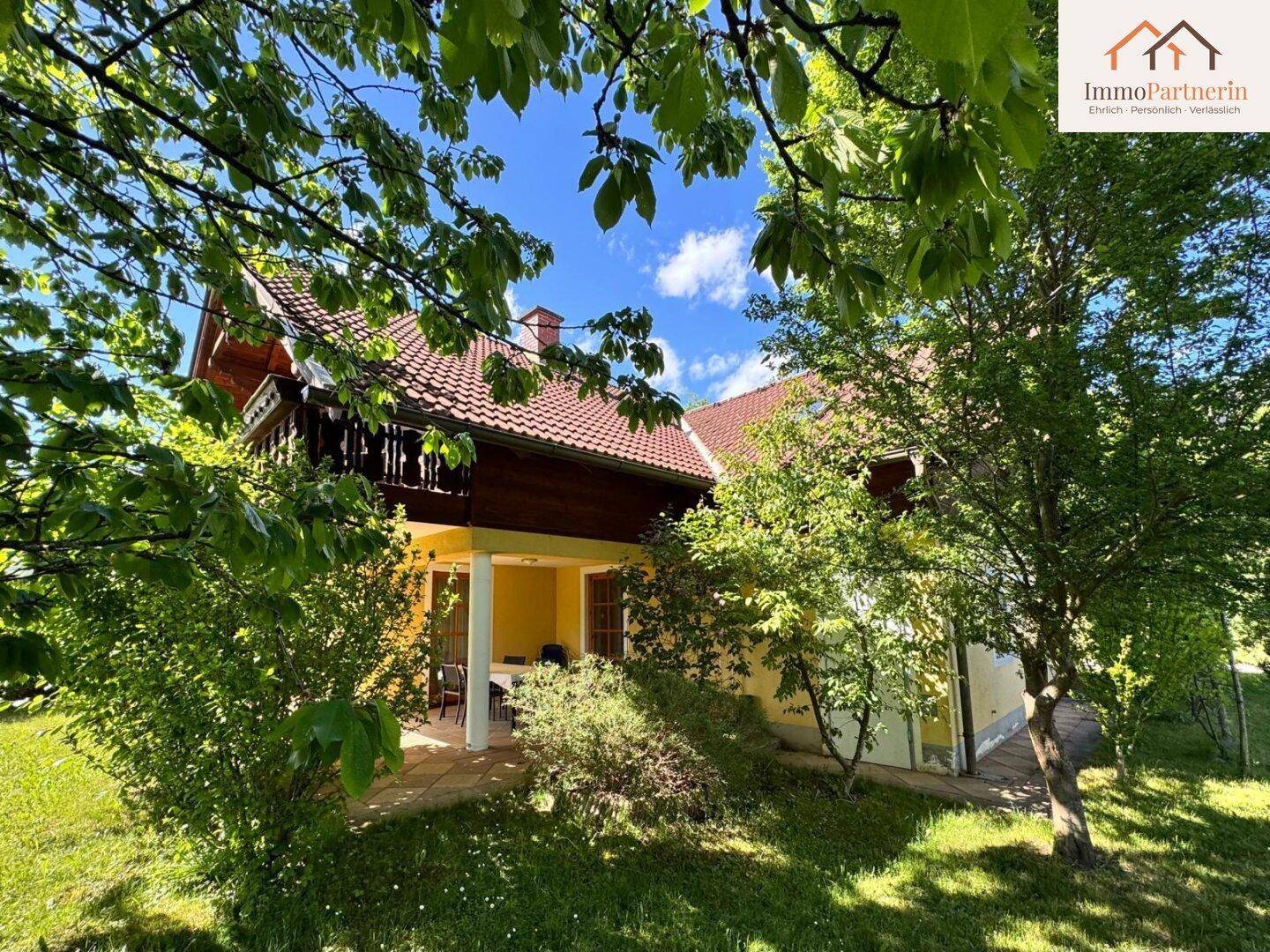 Überdachte Terrasse mit Gartenmöbeln, umgeben von Bäumen und viel Grün, ideal für entspannte Stunden.