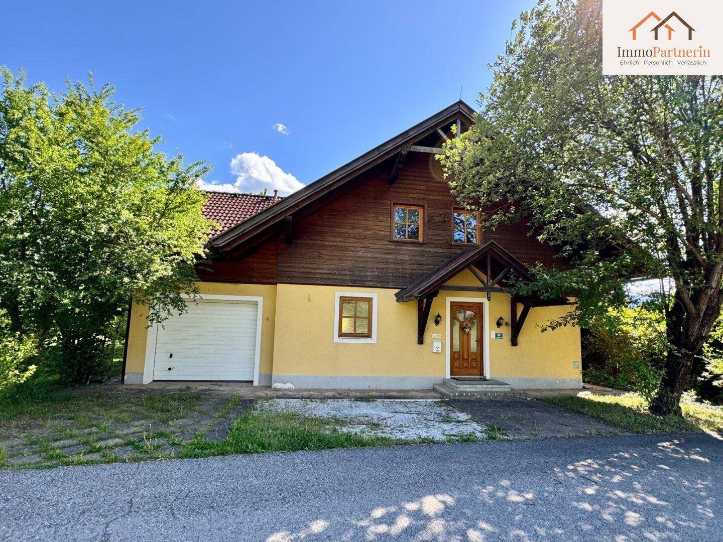 Attraktive Hausfassade mit integrierter Garage, gelbem Putz und Holzelementen im Obergeschoss.