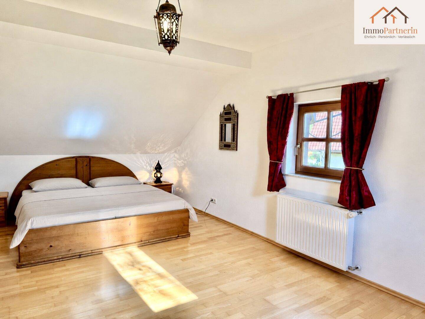 Geräumiges Schlafzimmer mit Holzbett, Holzboden und einem Fenster, das viel Licht spendet.
