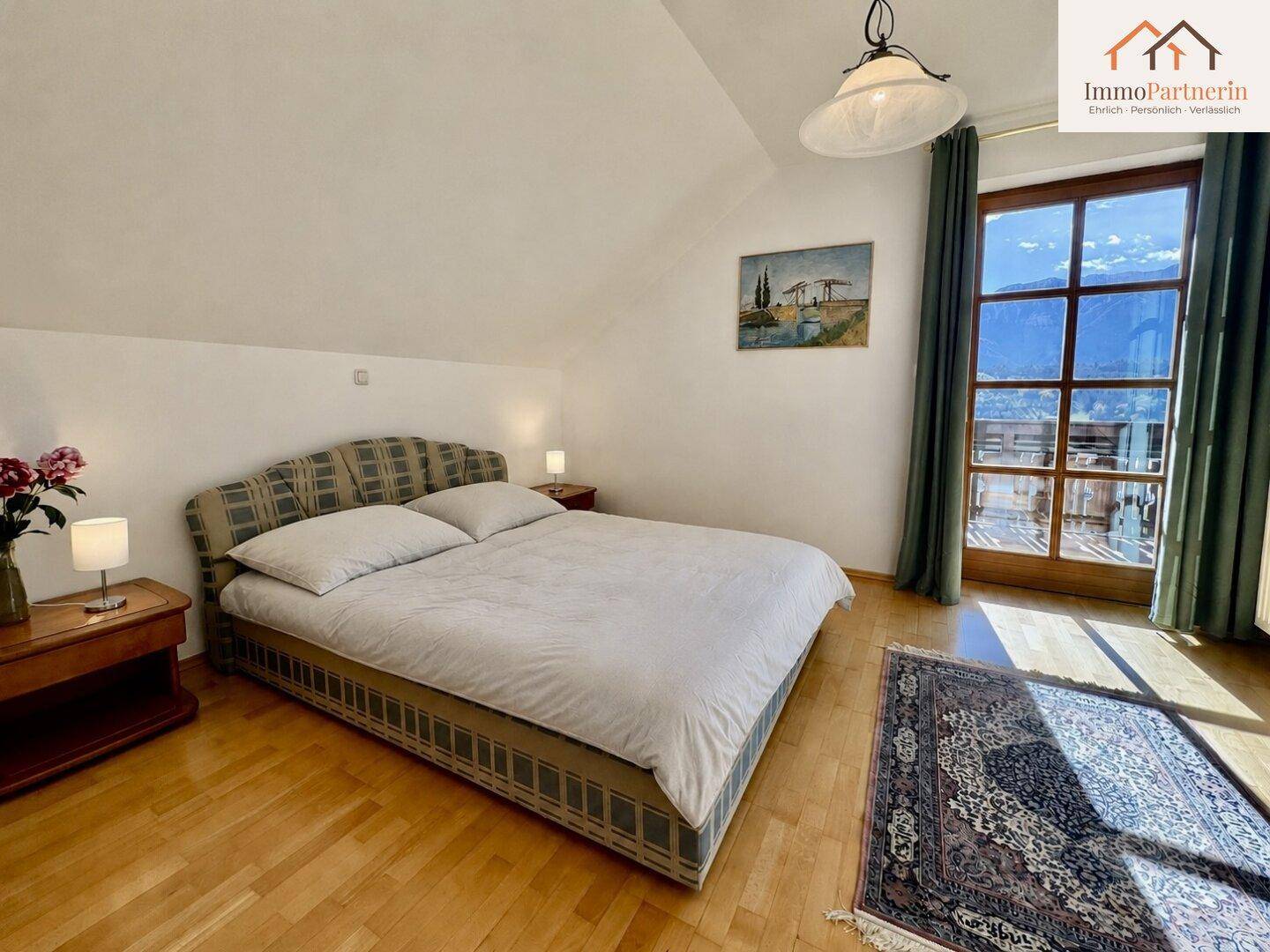 Helles Schlafzimmer mit Holzboden, Dachschräge und Zugang zu einem Balkon mit schöner Aussicht.
