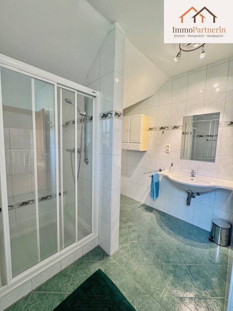 Helles Badezimmer mit Duschkabine, Einzelwaschbecken und Fliesen in Grün und Weiß.