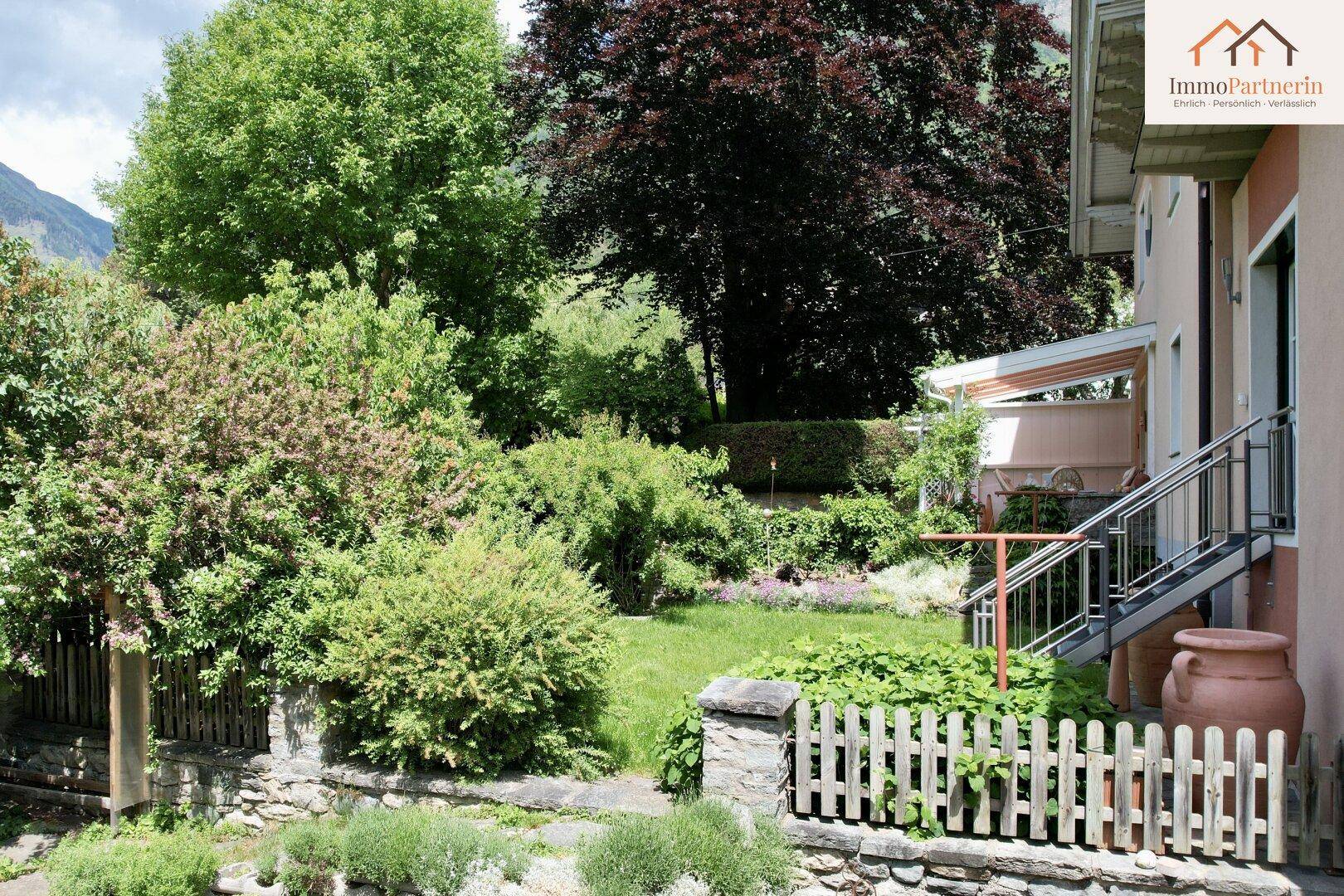Großer, gepflegter Garten mit Rasen, Sträuchern und Zugang zum Haus über eine Treppe.