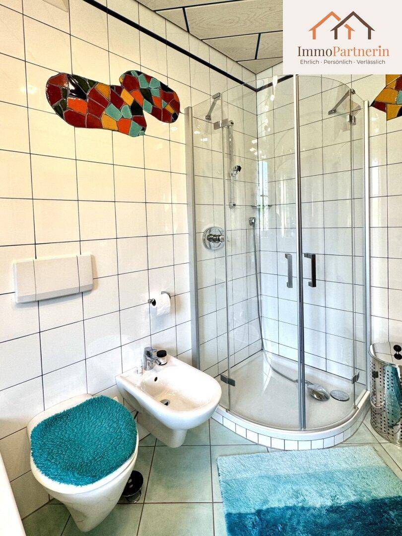 Gefliestes Badezimmer mit Duschkabine, WC, Bidet und farbenfrohen Akzenten.