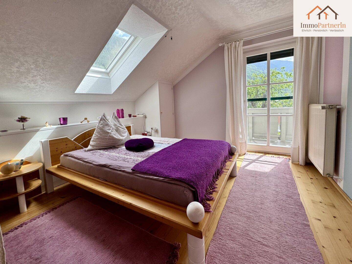 Dachschlafzimmer mit Holzbett, Dachfenster und Zugang zu einem französischen Balkon.