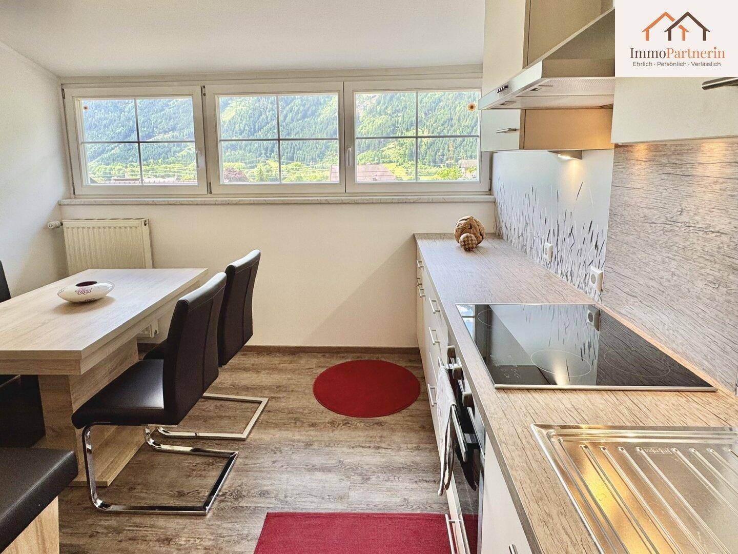 Moderne Küche mit Essbereich, Holzoptik-Arbeitsplatten und Blick auf die Berge.