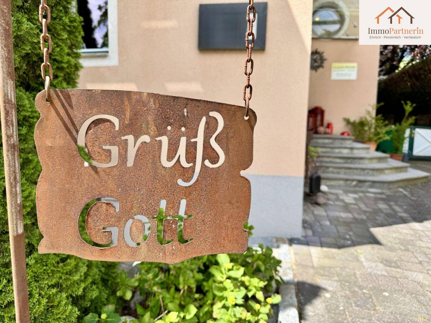 Rustikales 'Grüß Gott'-Schild aus Metall am Eingangsbereich des Hauses.