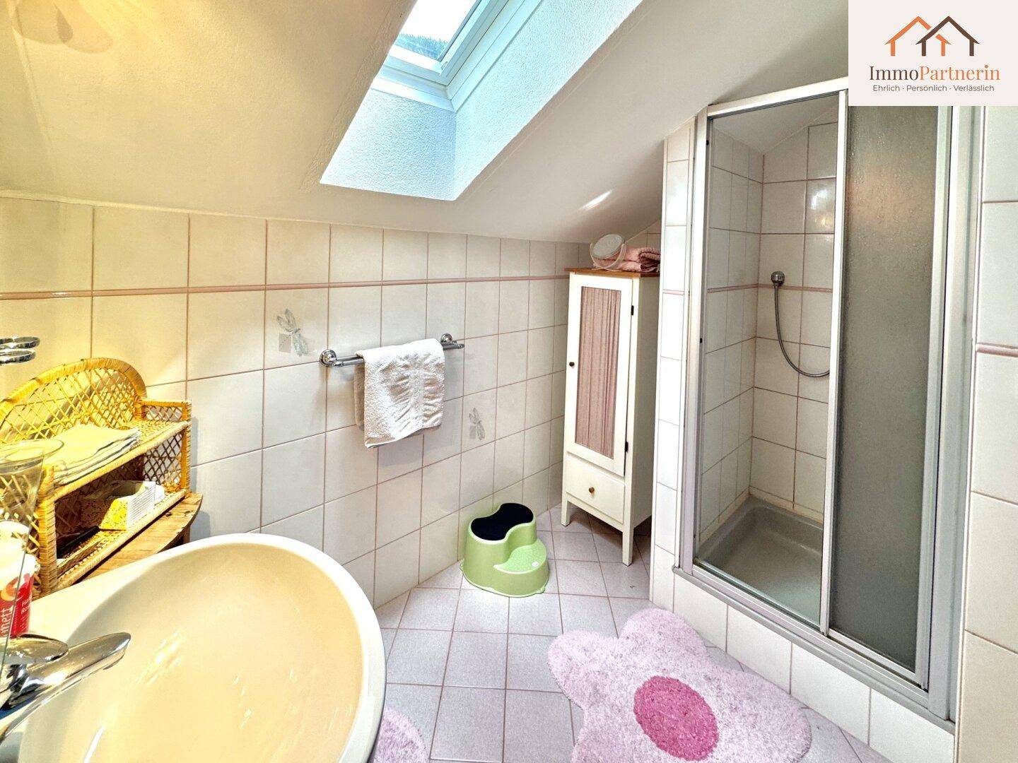 Helles Badezimmer im Dachgeschoss mit Duschkabine, Waschbecken und Dachfenster.