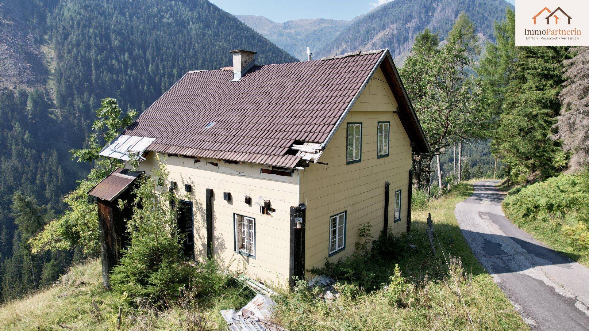 Älteres Haus in den Bergen mit beschädigtem Dach und umgebender Natur.