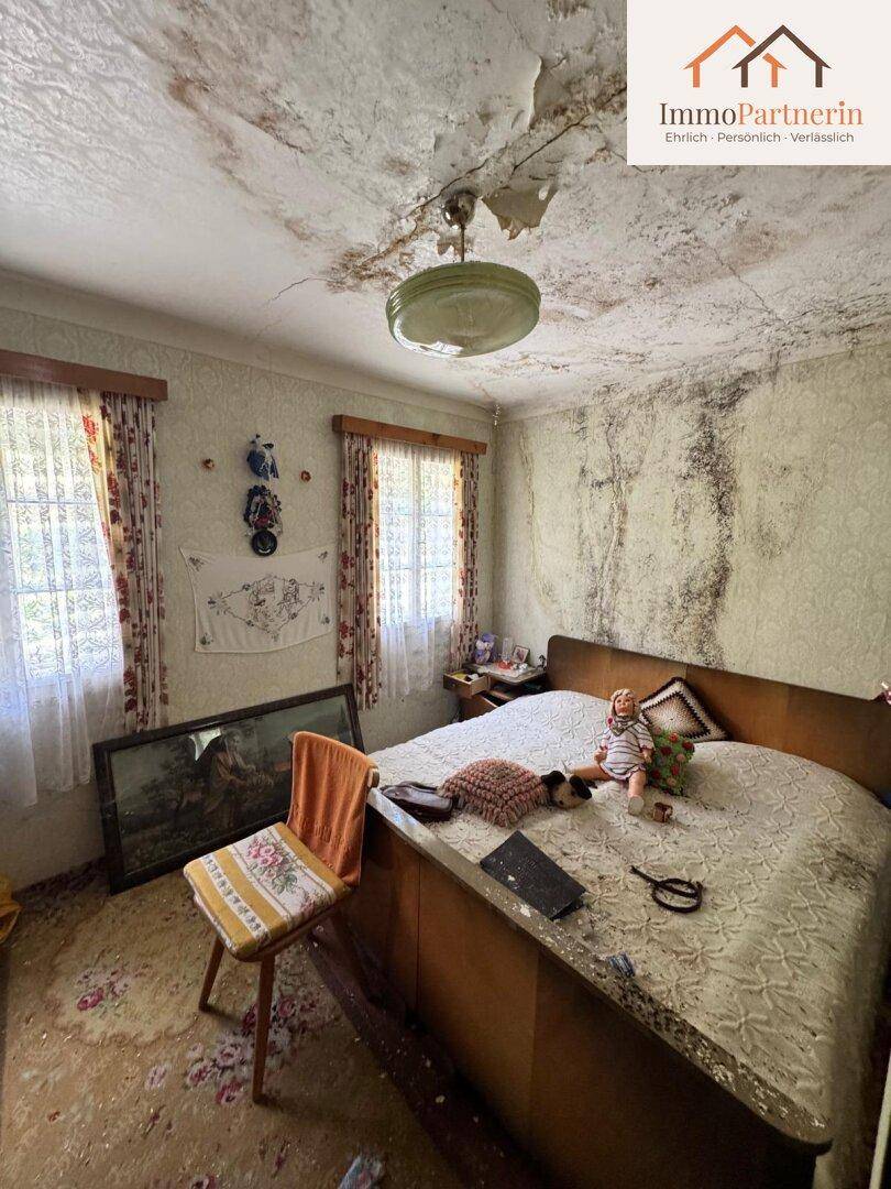 Schlafzimmer mit stark beschädigter Decke, alten Möbeln und schimmeligen Wänden.