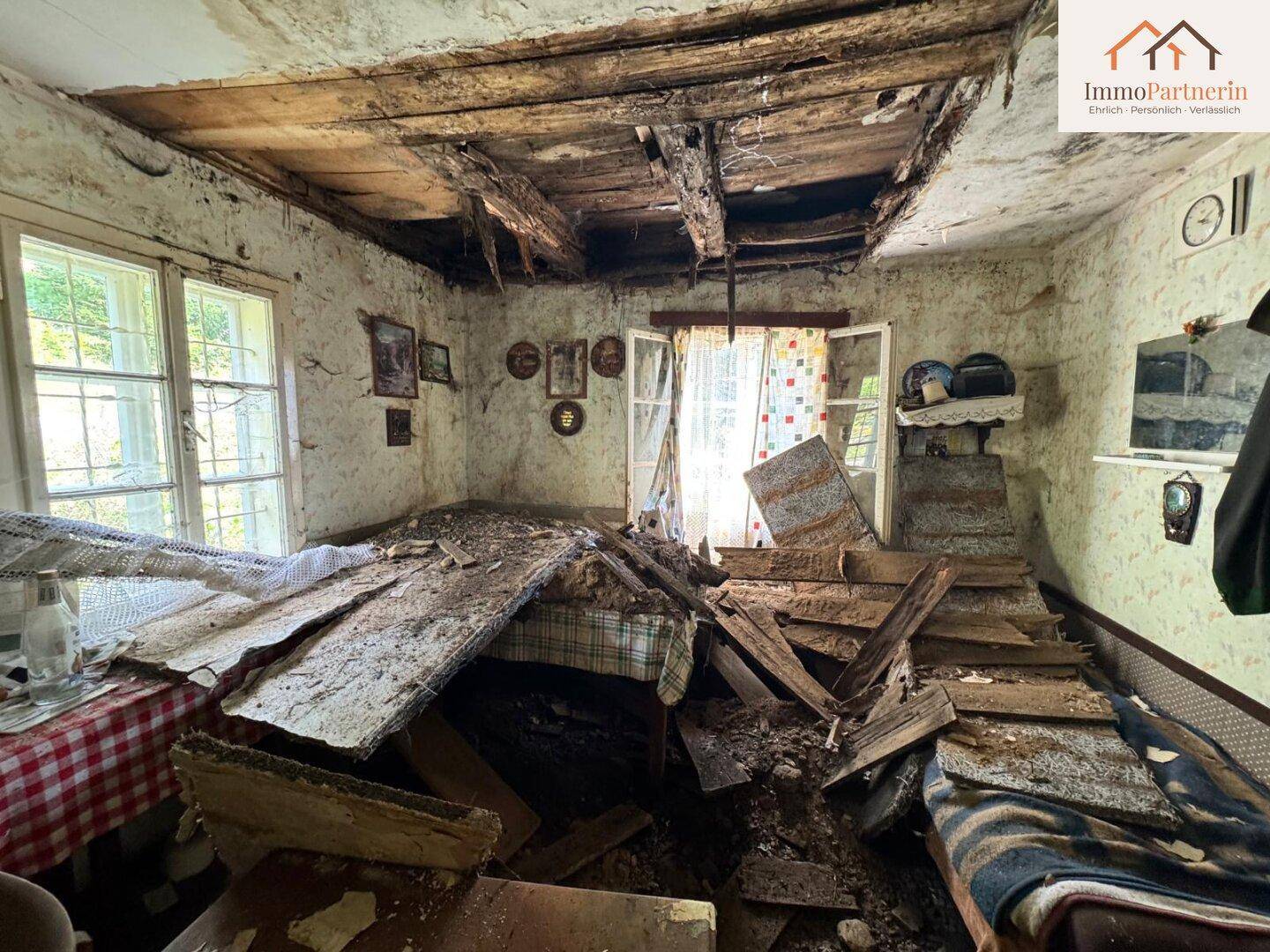 Stark beschädigtes Schlafzimmer mit eingestürzter Decke und Trümmern auf dem Boden.