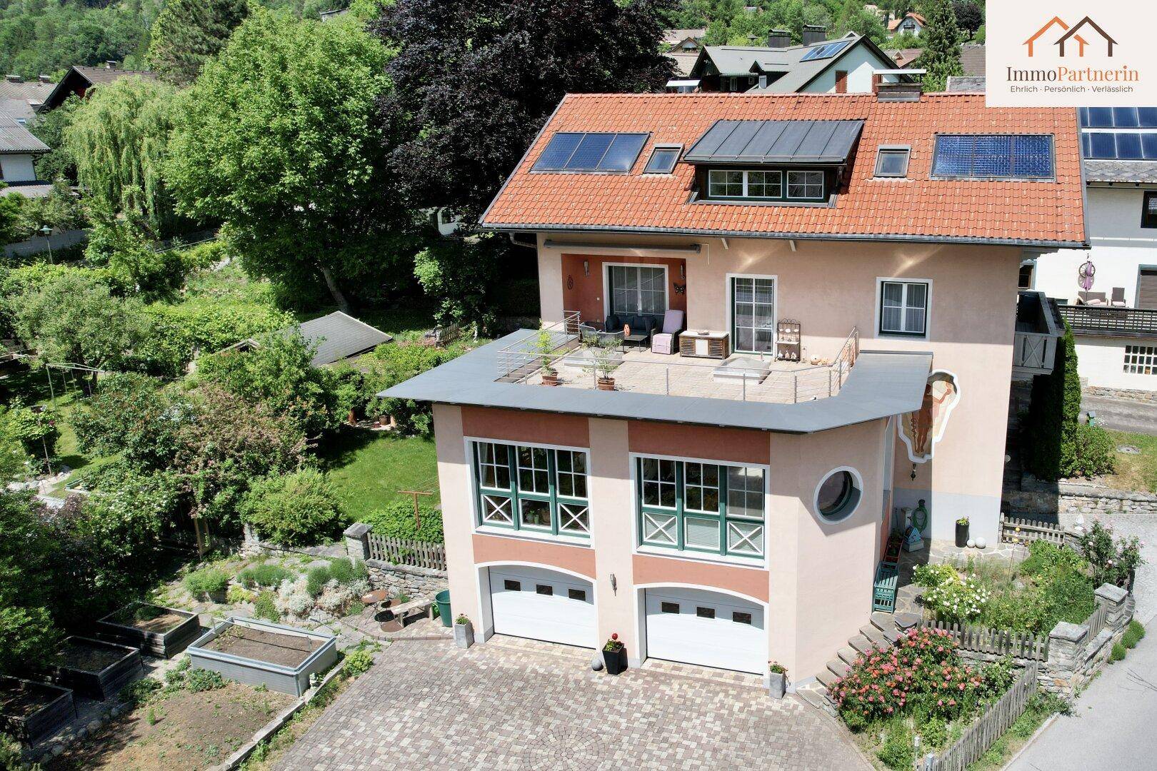 Luftaufnahme eines gepflegten Hauses mit großer Sonnenterrasse, Doppelgarage und weitläufigem Garten.