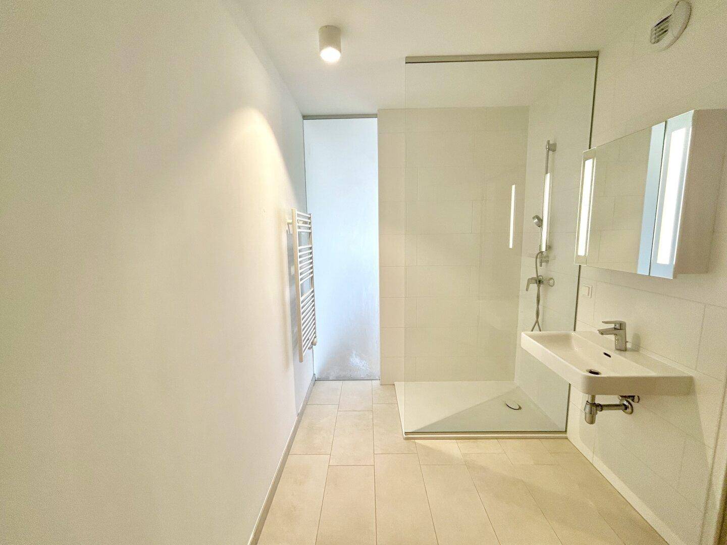 Helles Badezimmer mit moderner begehbarer Dusche, Waschtisch und beleuchtetem Spiegelschrank.