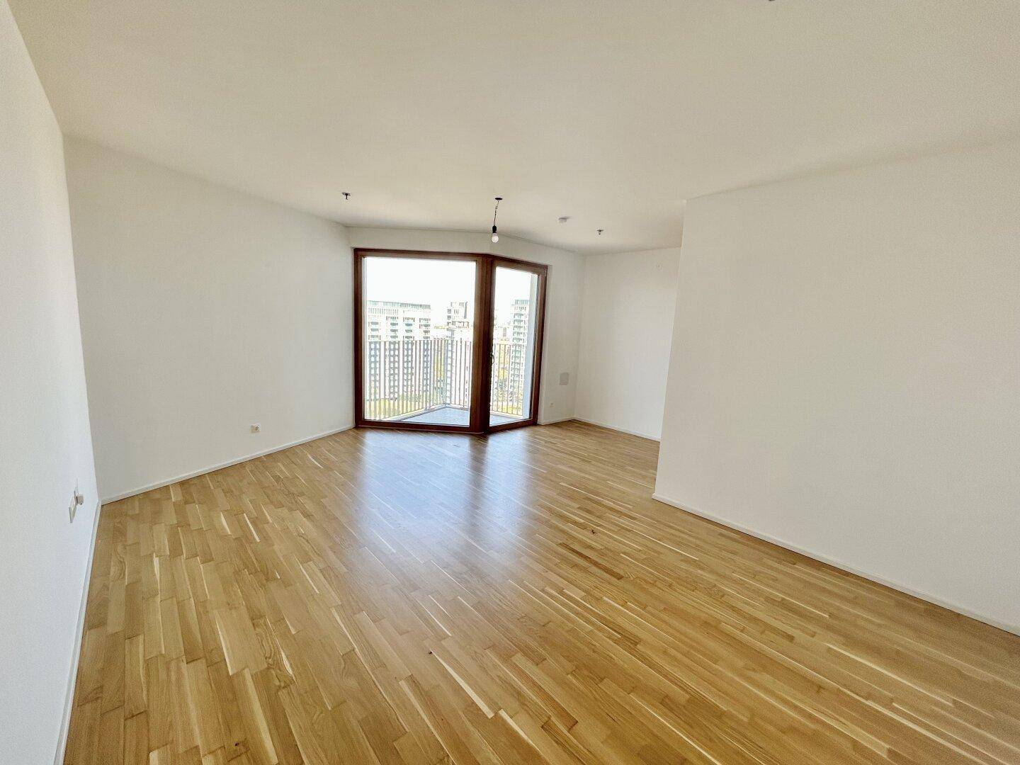 Geräumiges Wohnzimmer mit Parkettboden und großen Fenstern, die viel Licht hereinlassen.