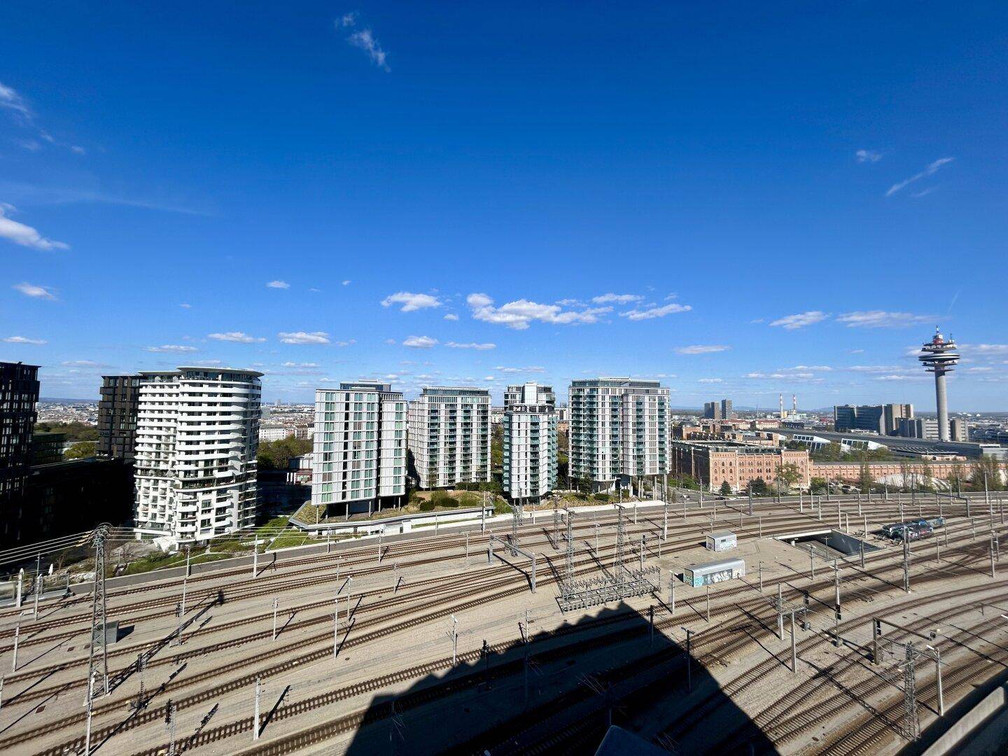 Panoramablick über die Stadt mit Hochhäusern, Bahngleisen und einem markanten Turm.