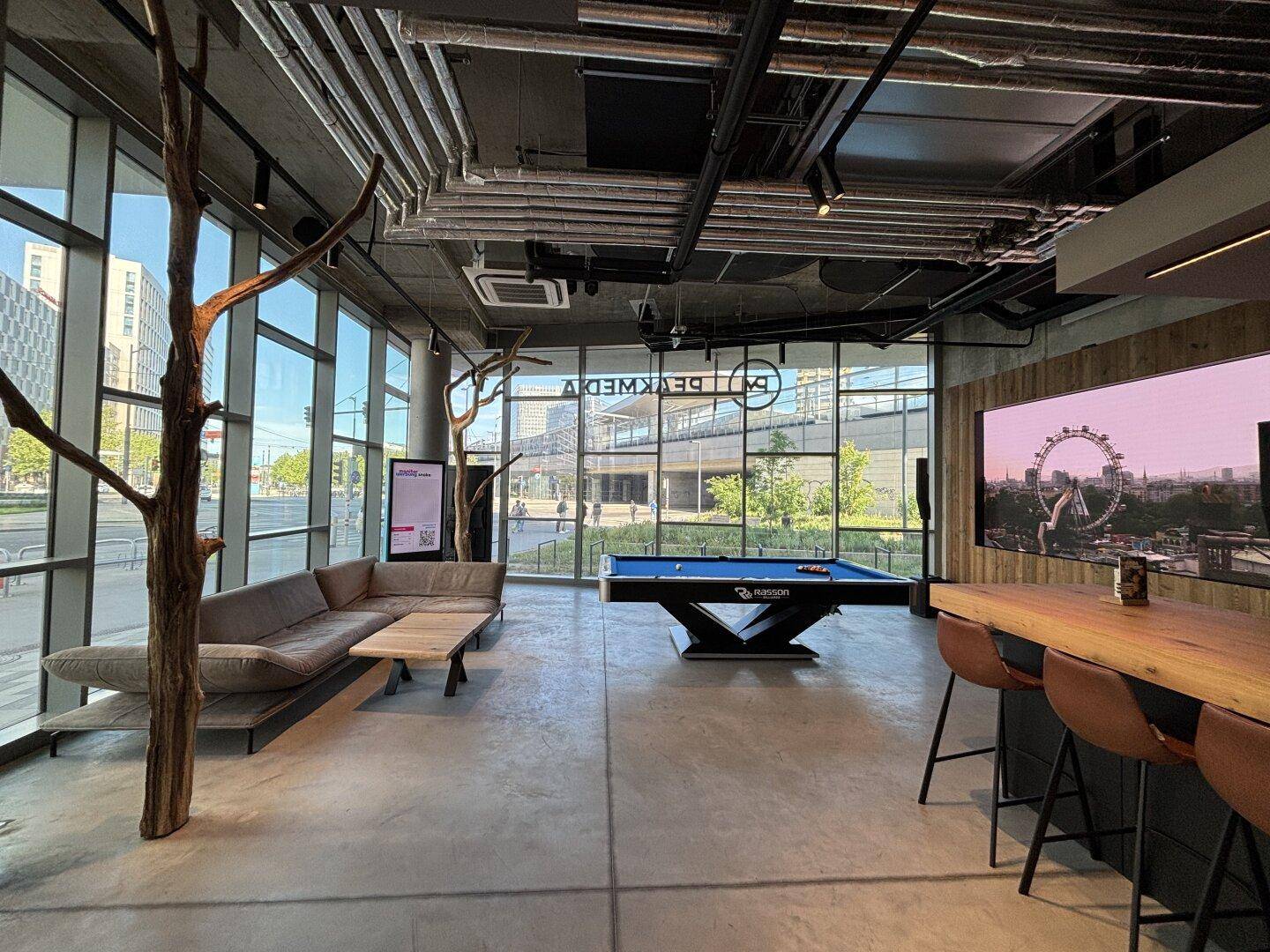 Moderner Loungebereich mit Billardtisch, bequemen Sofas und großen Fenstern mit Stadtblick.