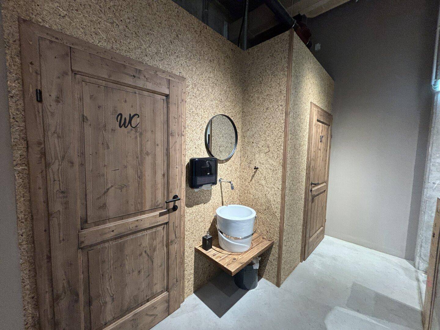 Rustikale Gästetoilette mit Holztüren und OSB-Plattenwänden, ausgestattet mit einem einfachen Waschbecken.