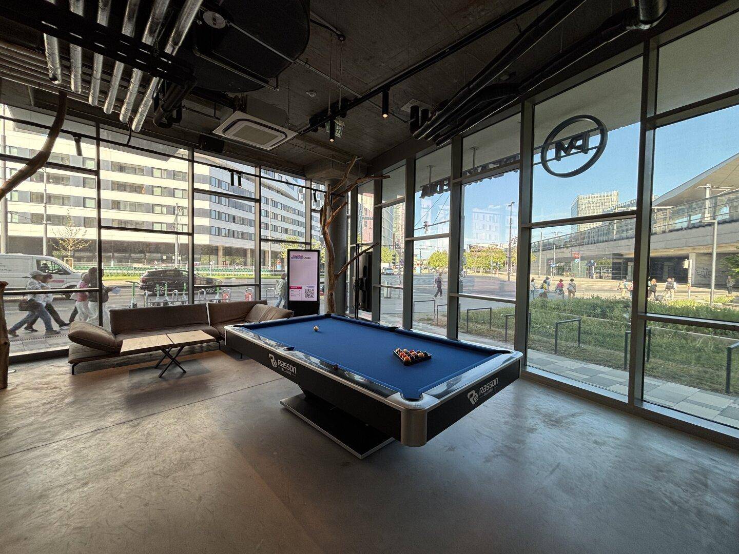 Heller Loungebereich mit Billardtisch, bequemen Sofas und großen Fenstern mit Stadtblick.