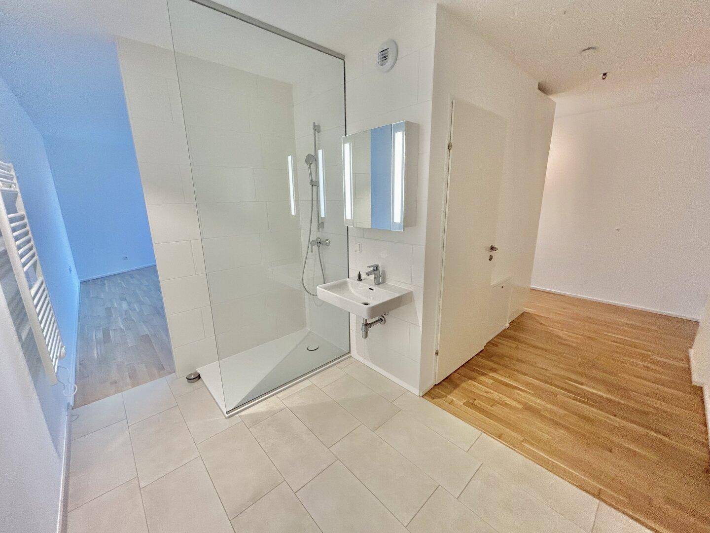 Helles Badezimmer mit großer Glasdusche, modernem Waschtisch und Fliesenboden.