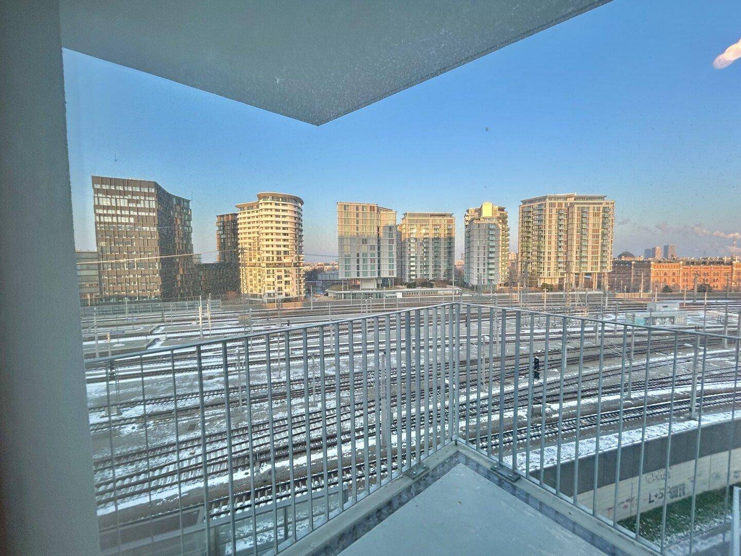 Balkon mit weitem Blick auf die Stadt, Bahngleise und moderne Hochhäuser am Horizont.