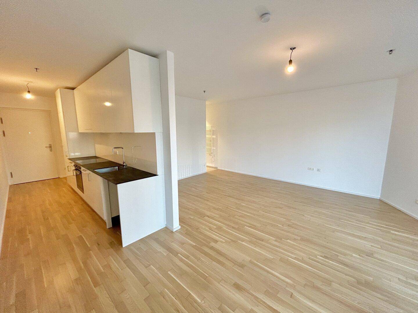 Offener Wohnbereich mit integrierter moderner Küche und hellem Parkettboden, ideal für geselliges Beisammensein.