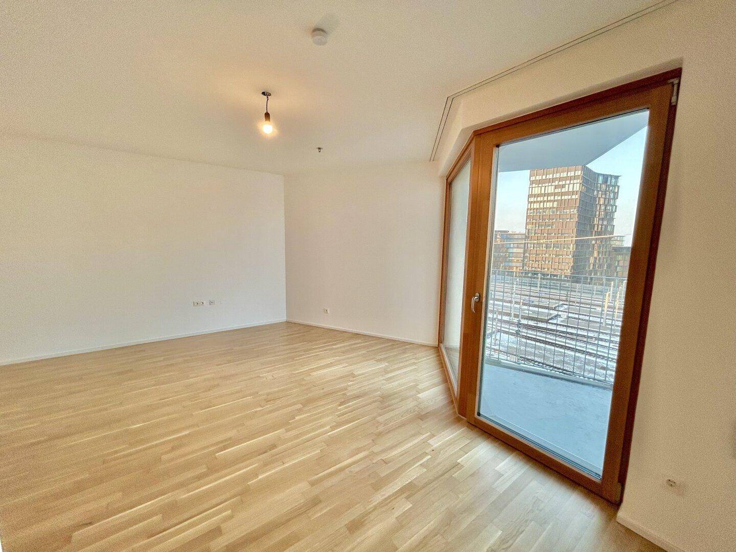 Heller Wohnbereich mit Parkettboden und großem Fenster, das viel Tageslicht hereinlässt.