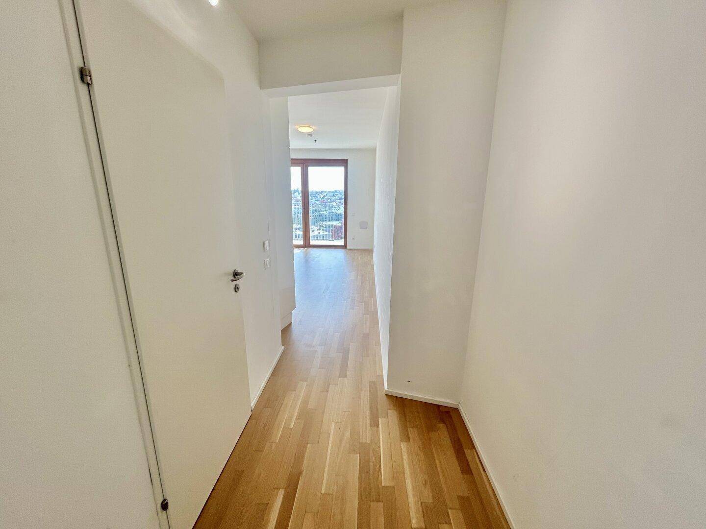 Langer Flur mit Holzboden, der in einen hellen Wohnbereich mit Stadtblick mündet.