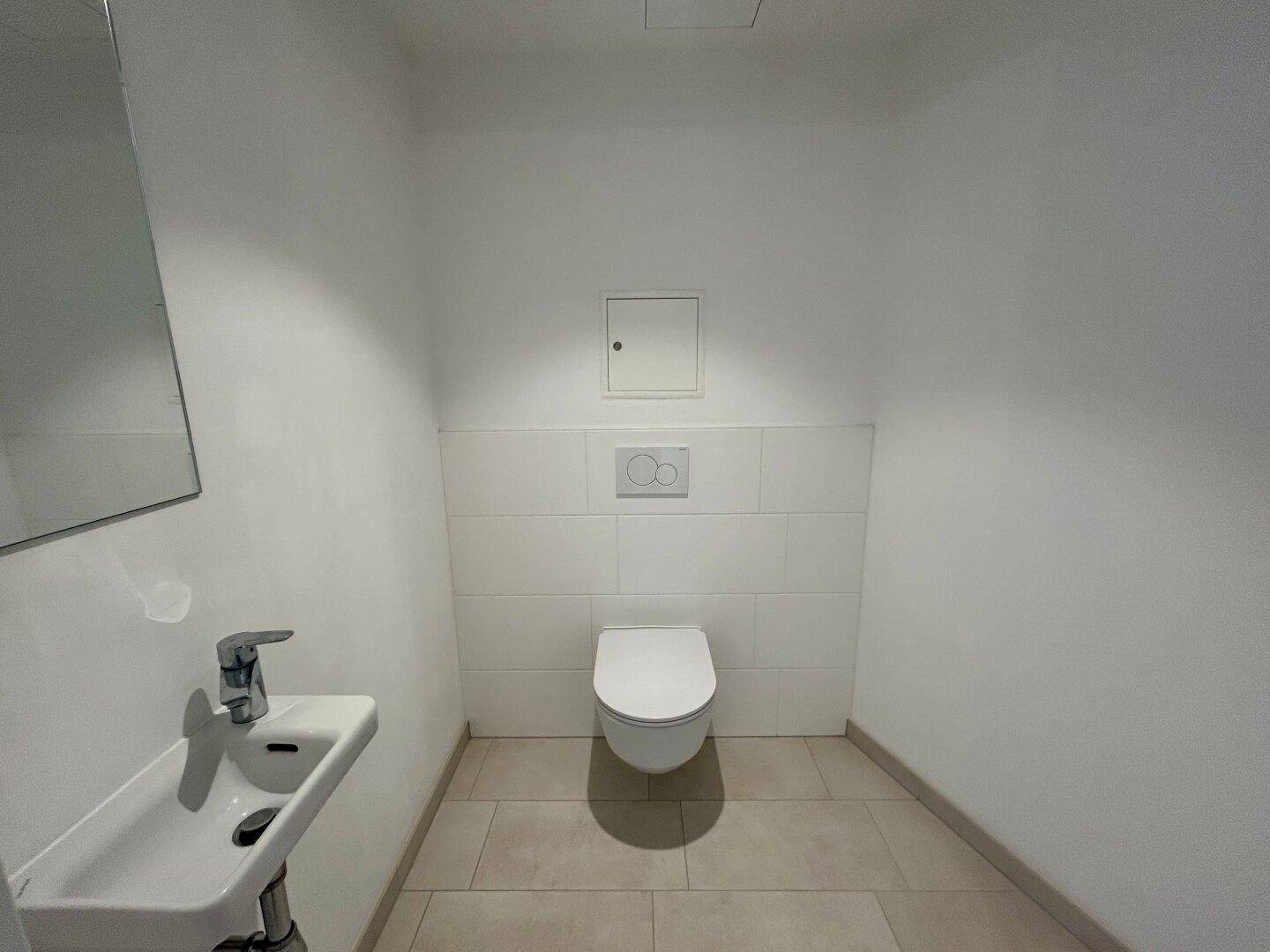 Modernes Gäste-WC mit wandhängender Toilette, kleinem Waschbecken und hellen Fliesen.