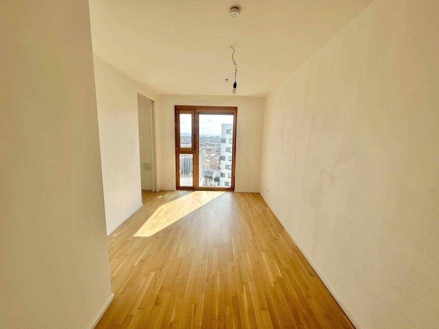 Helles Schlafzimmer mit Parkettboden, großen Fenstern und Zugang zu einem Balkon.