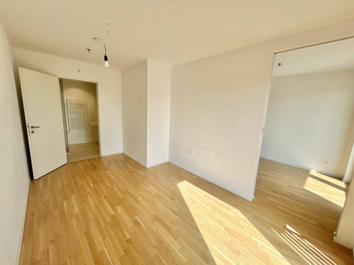 Geräumiges Schlafzimmer mit hellem Parkettboden und direktem Zugang zu einem Badezimmer.