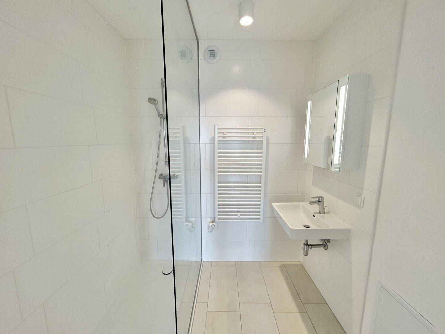 Modernes Badezimmer mit ebenerdiger Dusche, Waschbecken und beheiztem Handtuchhalter.