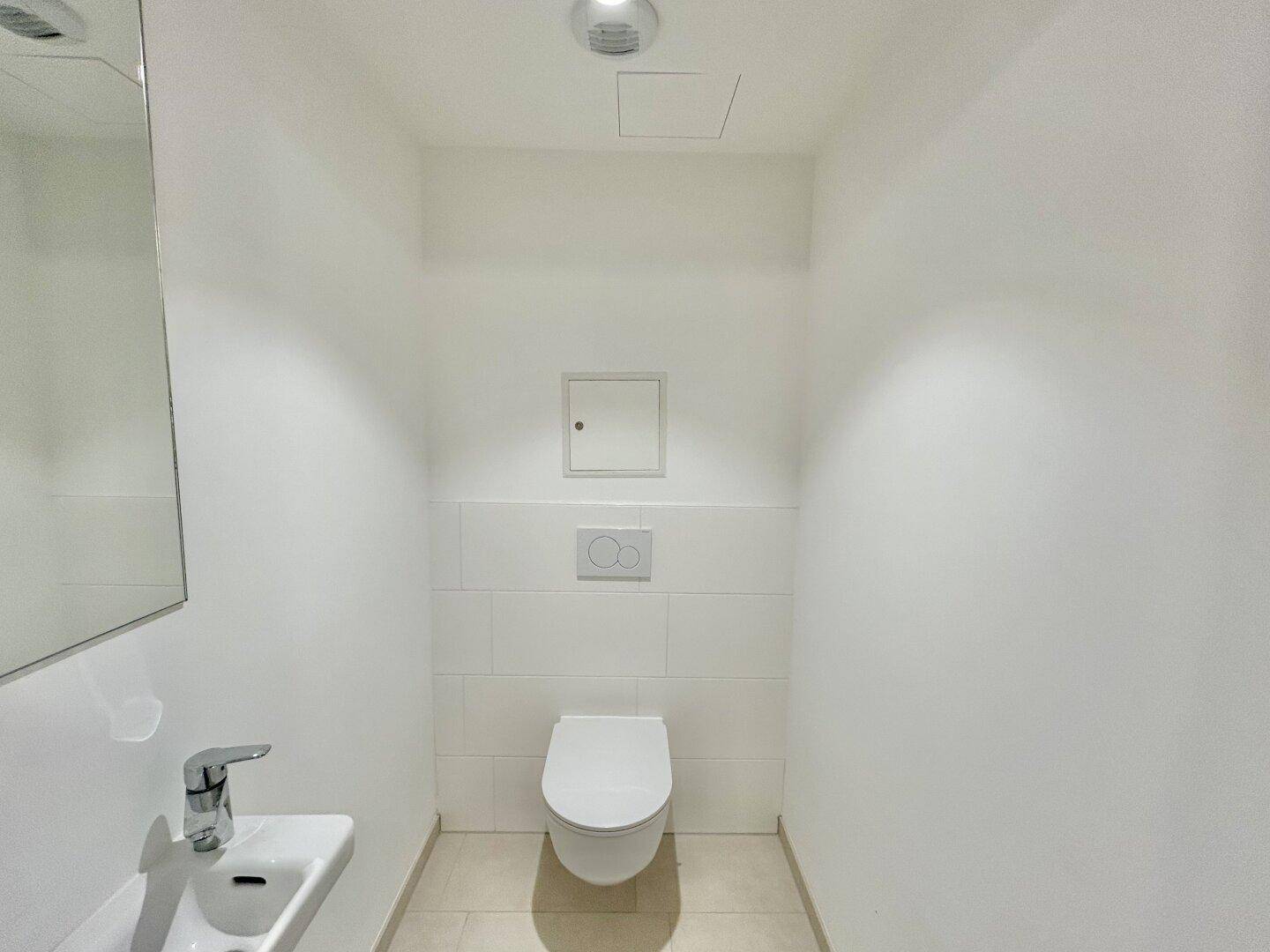 Modernes Gäste-WC mit wandhängender Toilette, kleinem Waschbecken und hellen Fliesen.