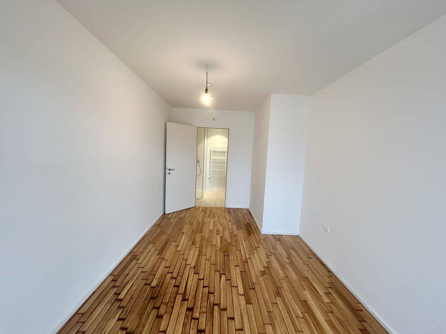 Geräumiges Schlafzimmer mit Holzboden und weiß gestrichenen Wänden, angrenzend an ein Badezimmer.