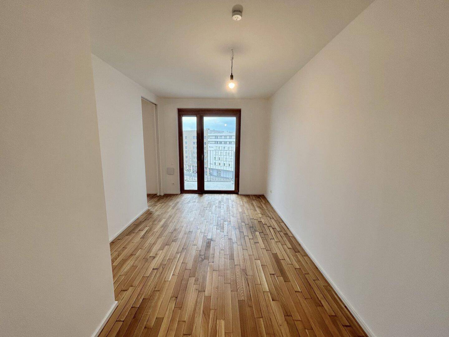 Lichtdurchfluteter Raum mit Parkettboden und großer Fensterfront, ideal als Schlaf- oder Arbeitszimmer.