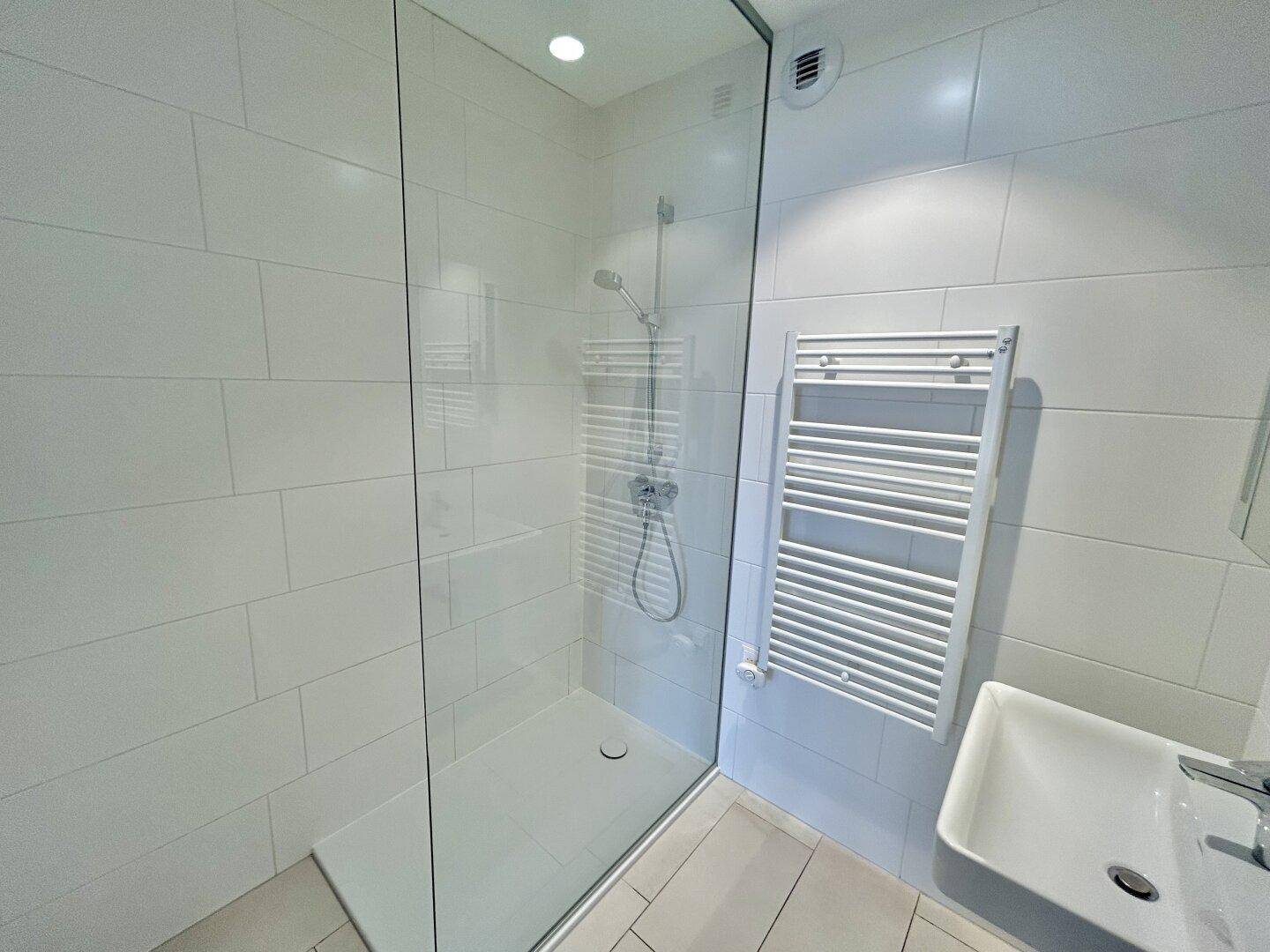 Ebenerdige Dusche mit Glasabtrennung und weißen Fliesen im modernen Badezimmer.