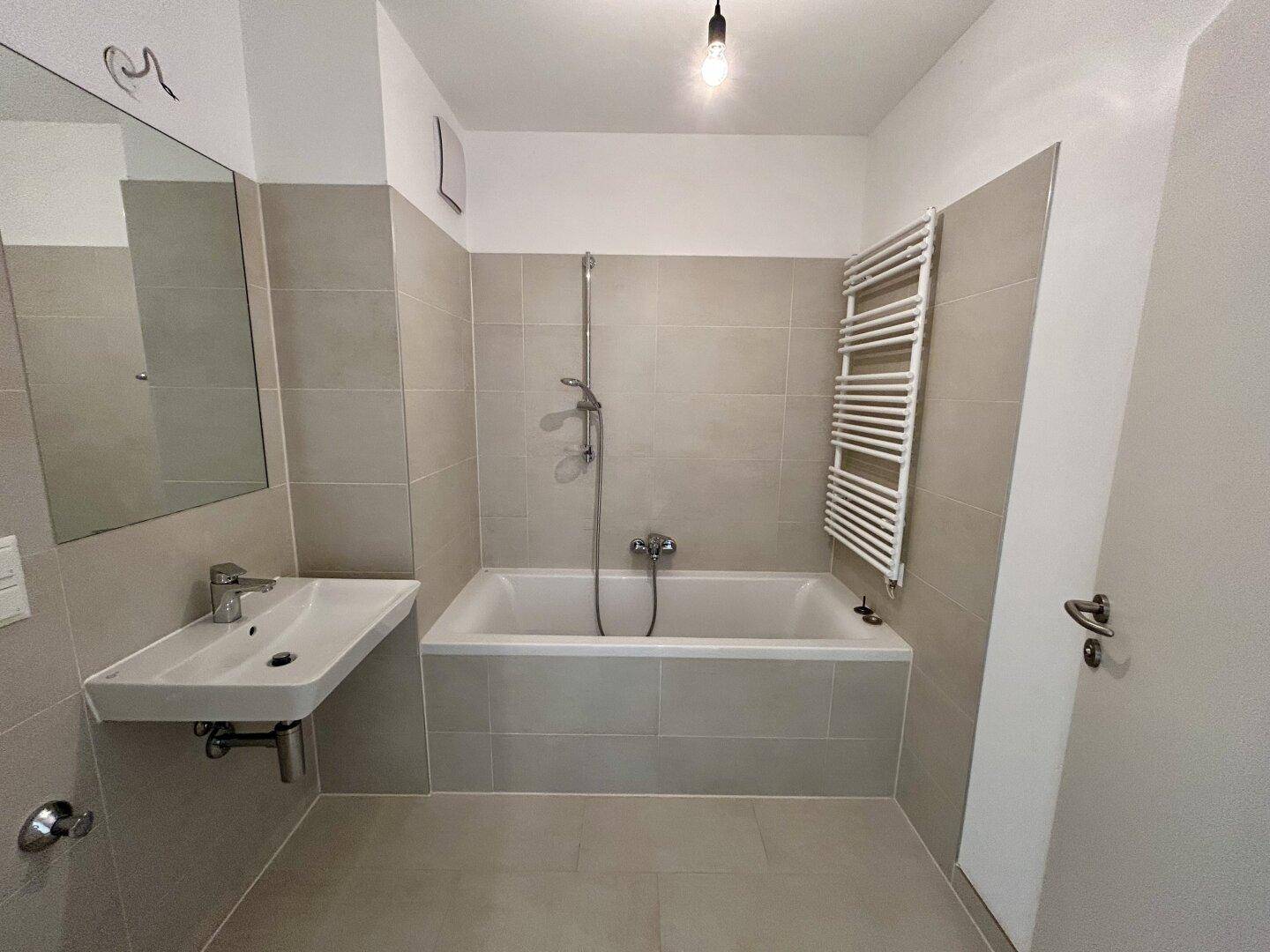 Modernes Badezimmer mit Badewanne, Einzelwaschbecken und beheiztem Handtuchhalter.