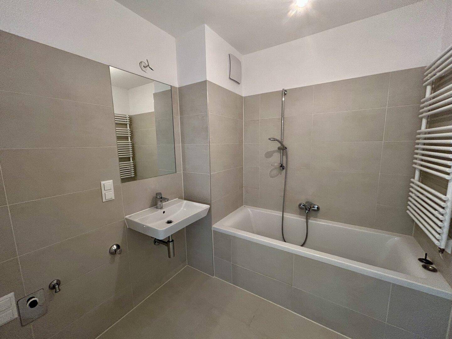 Zeitgemäßes Badezimmer mit Badewanne, Spiegel und grauen Fliesen, in neuwertigem Zustand.