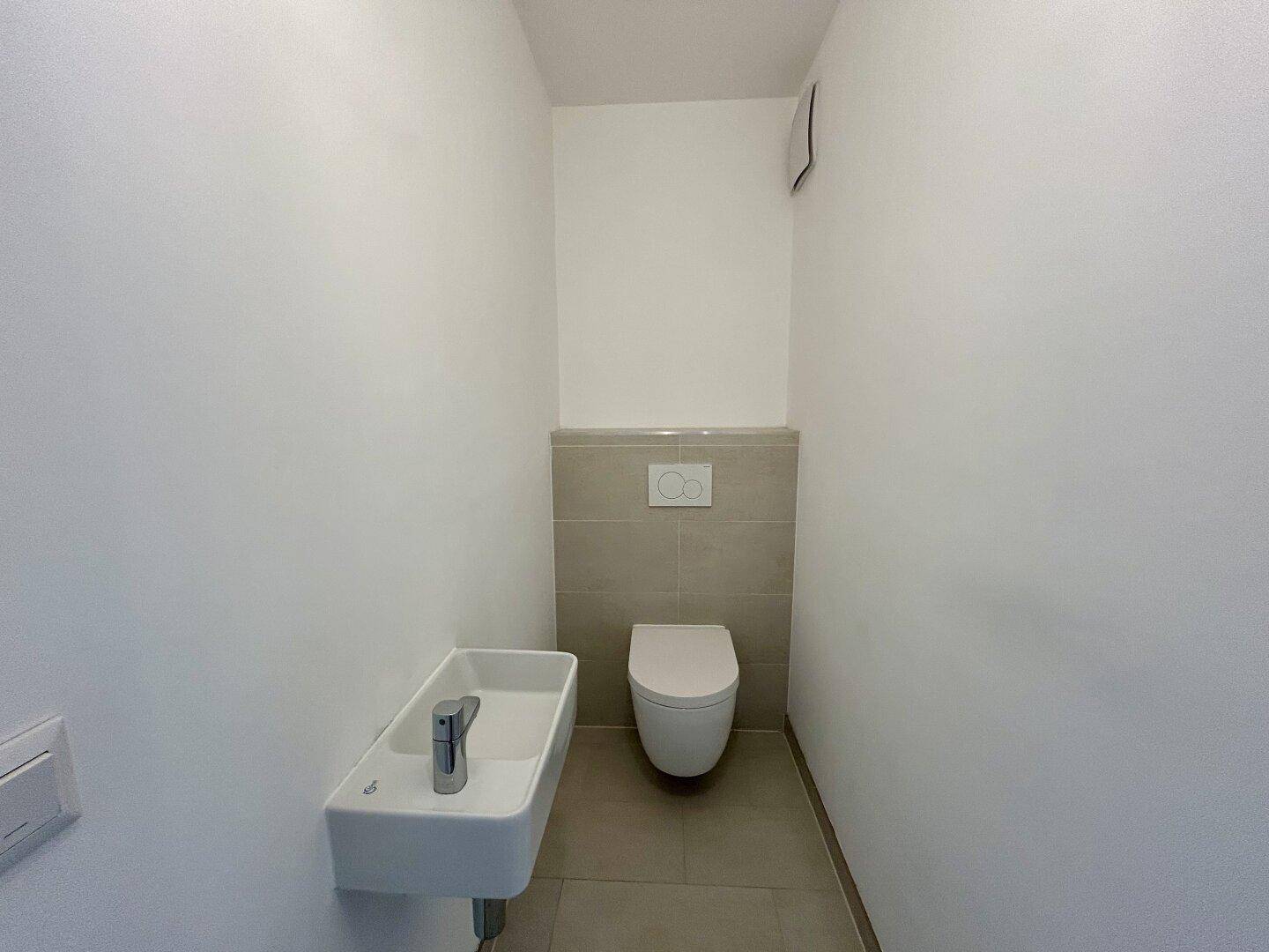Separates Gäste-WC mit wandhängender Toilette und kleinem Handwaschbecken.