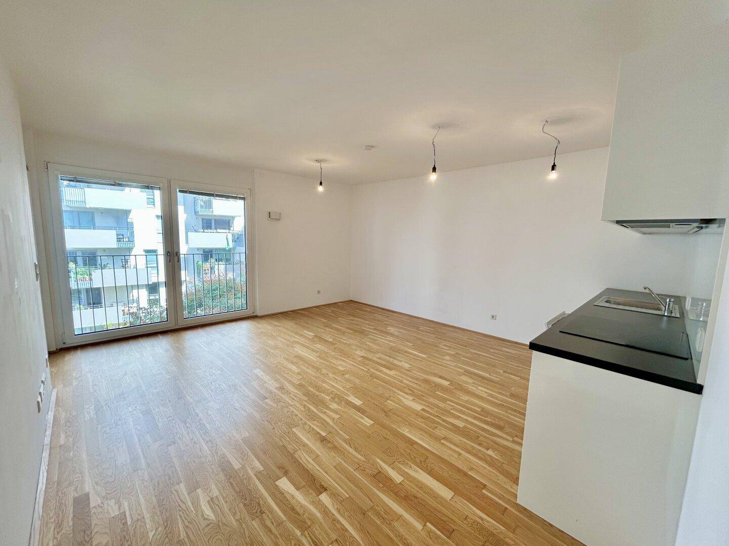 Offener Wohnbereich mit Parkettboden und Blick auf den Balkon, bereit für individuelle Gestaltung.
