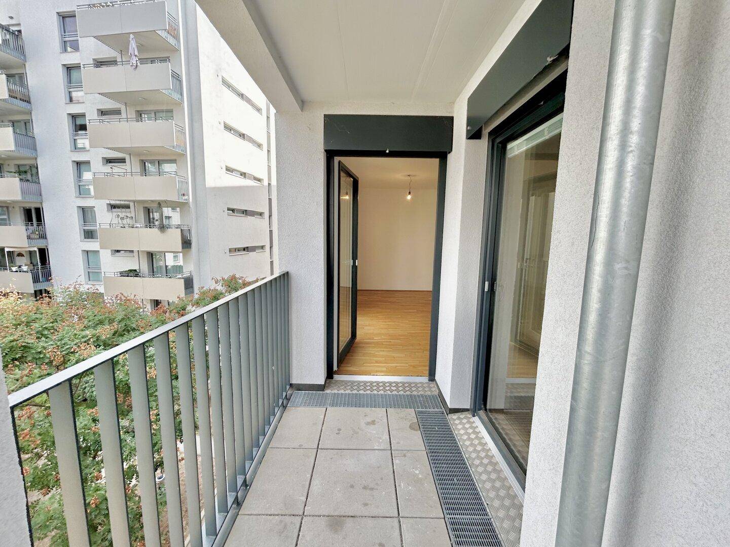 Balkon mit Fliesenboden und Zugang zum Innenraum, umgeben von moderner Architektur.